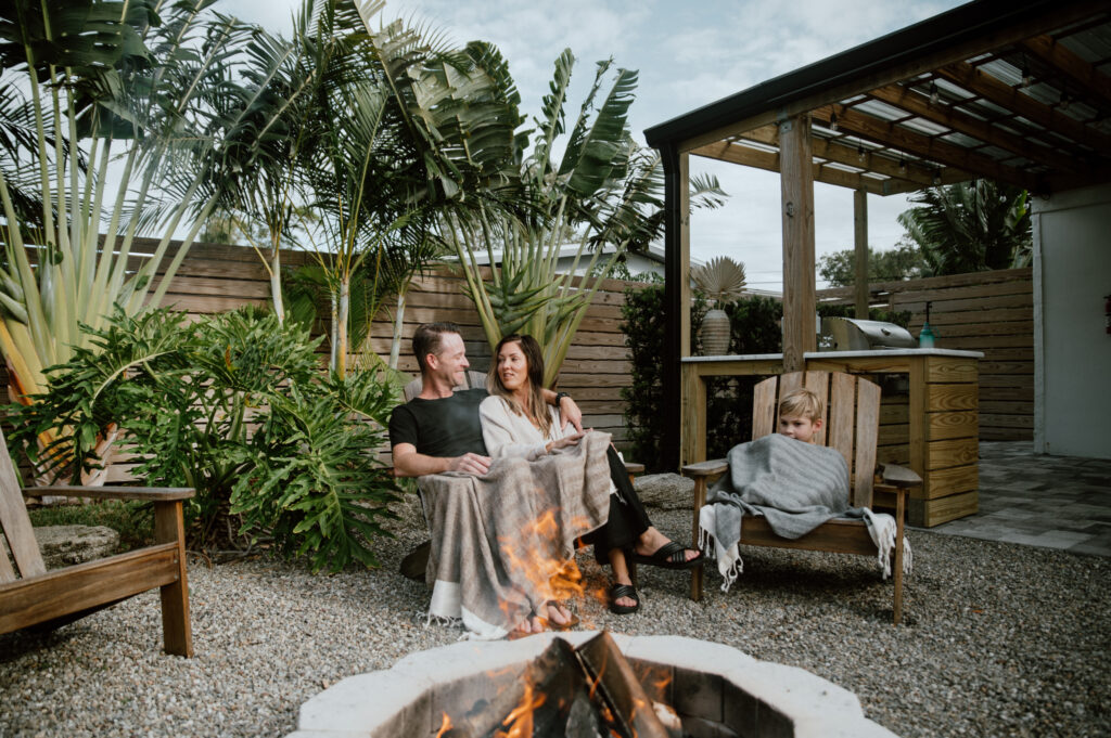 Friends gathered outdoors at a coastal vacation rental enjoying drinks and conversation under tropical trees