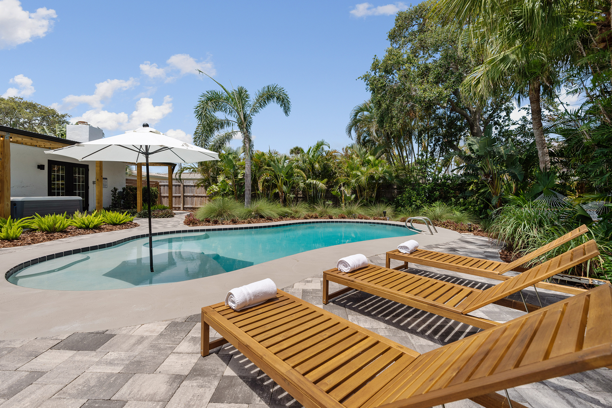 Pool and wooden loungers surrounded by palms at Coastal Scandinavian Retreat, an accessible vacation home in Cocoa Beach.