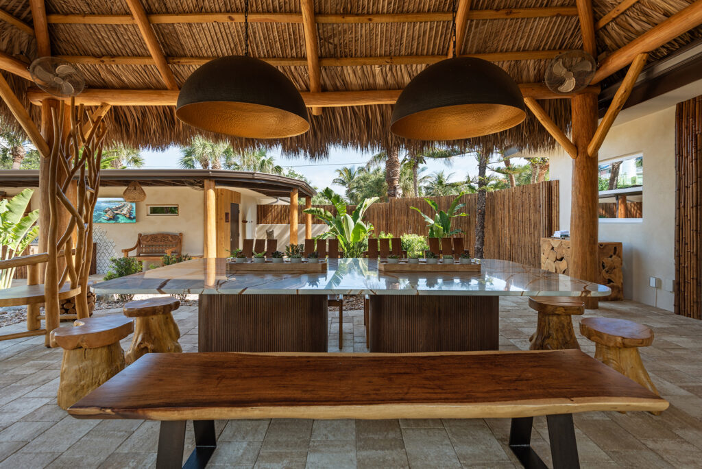 Spacious covered outdoor bar with wooden countertops, bar stools, hanging pendant lights, and natural wood beams