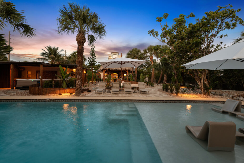 Evening view of The Maldivian in Cocoa Beach with palm trees, a lit swimming pool, lounge chairs, and umbrellas at dusk