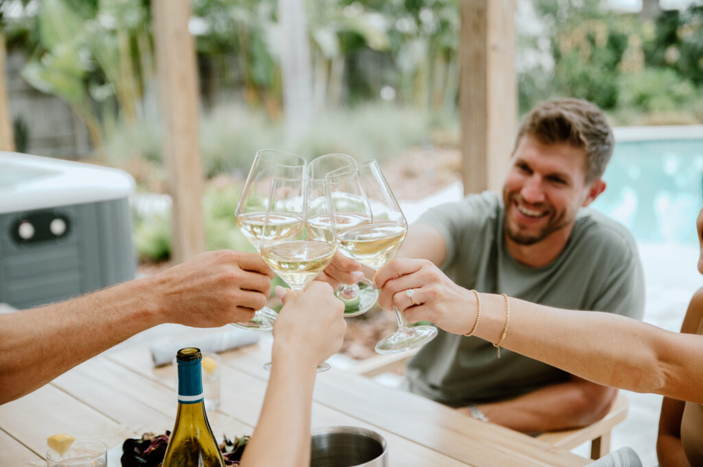 Friends clinking wine glasses together while sitting outdoors near a pool.