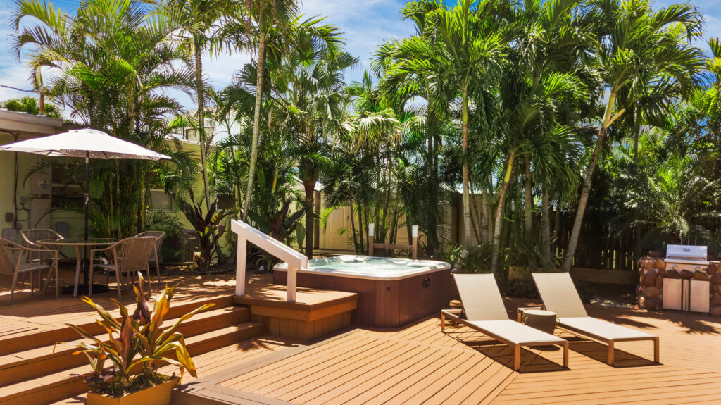 Outdoor lounge seating with cushioned benches, wooden furniture, and tropical palm trees at a coastal vacation rental