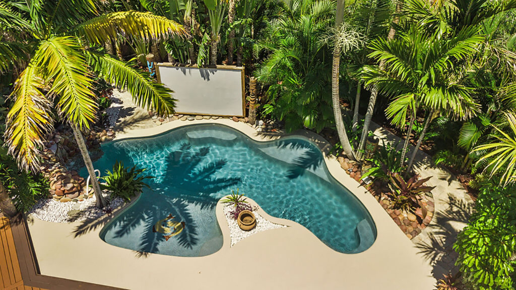 Tropical lagoon style pool surrounded by lush palm trees and greenery, with a sun shelf for lounging.