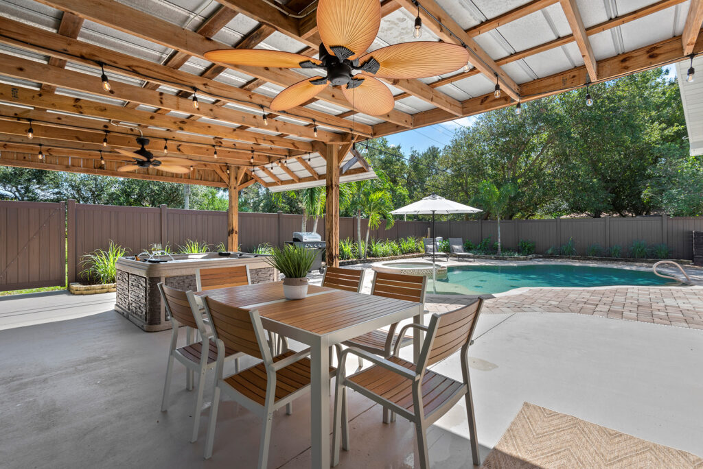 Outdoor dining area beneath a wooden pergola beside a private pool surrounded by lush trees in Cocoa Beach.
