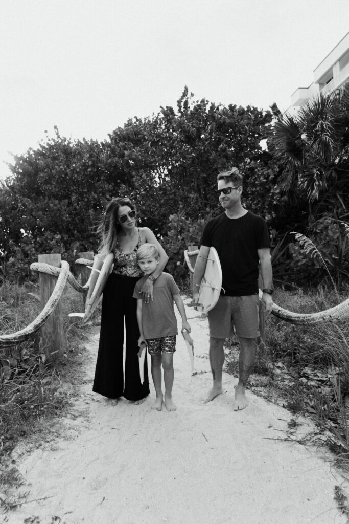 Black and white photo of a bride and groom walking down an outdoor aisle after their ceremony, surrounded by smiling guests