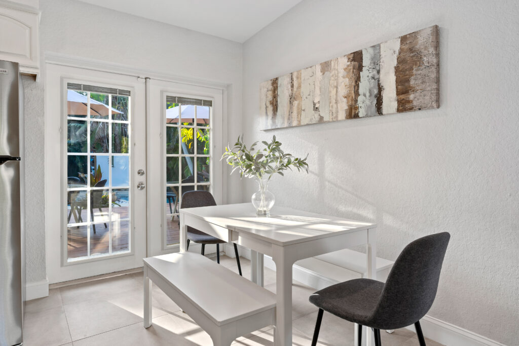 Bright breakfast nook with white furniture, soft natural light, and a view of a sunny outdoor patio.