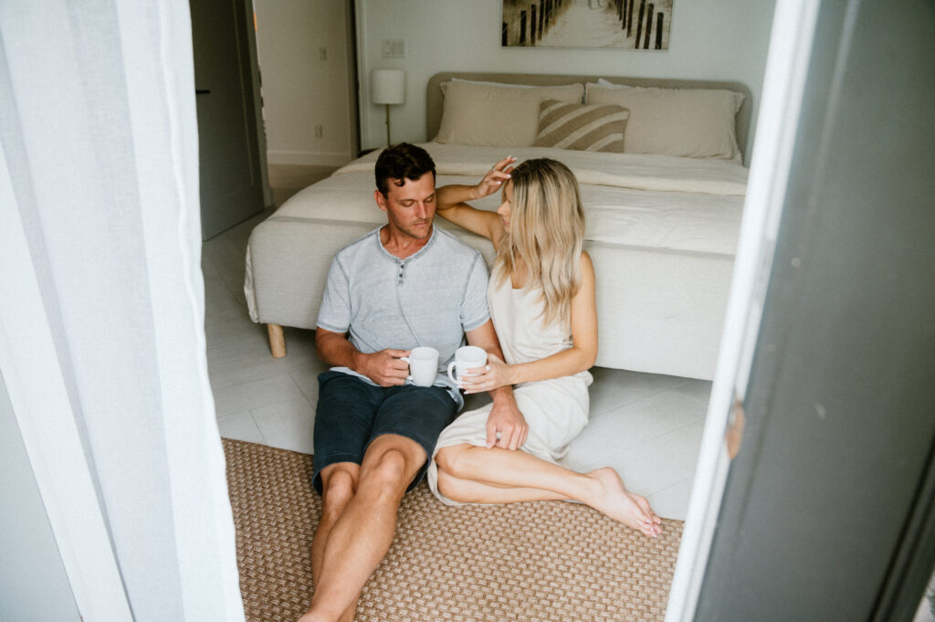 Couple sitting on the floor by their bed, sharing coffee and enjoying a quiet morning together.