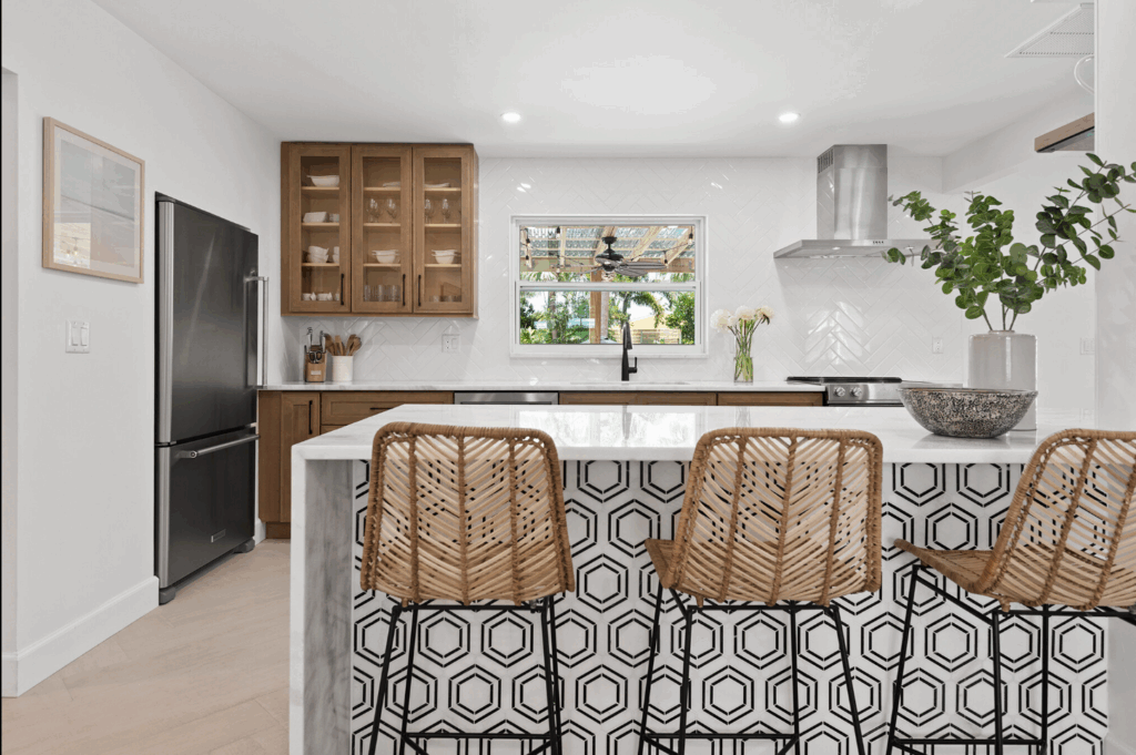 Modern kitchen with patterned island, woven barstools, wood cabinetry, and bright white walls accented by greenery.