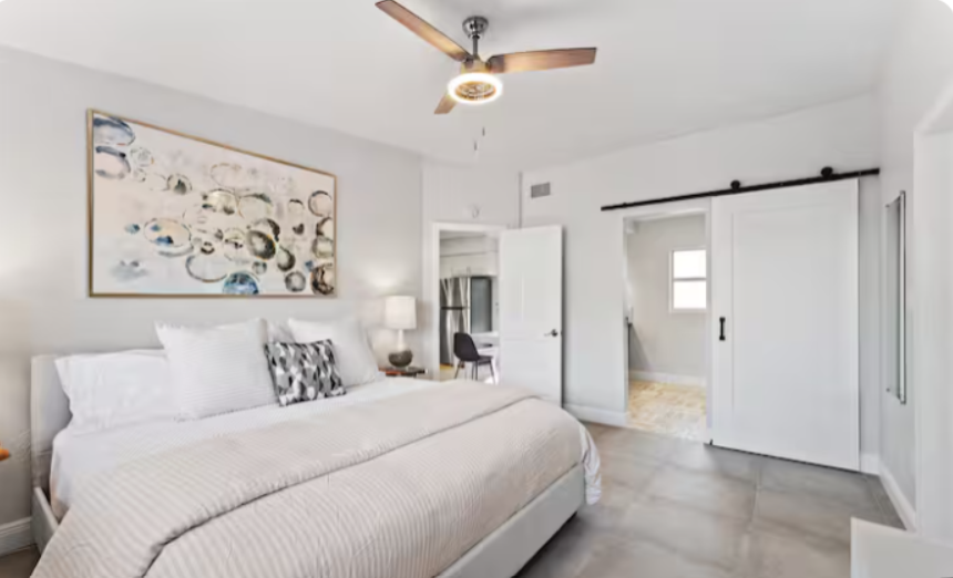 Bright coastal bedroom featuring a white bed, beach-inspired décor, luxury vinyl flooring, and a spacious layout designed for a relaxing Cocoa Beach getaway.
