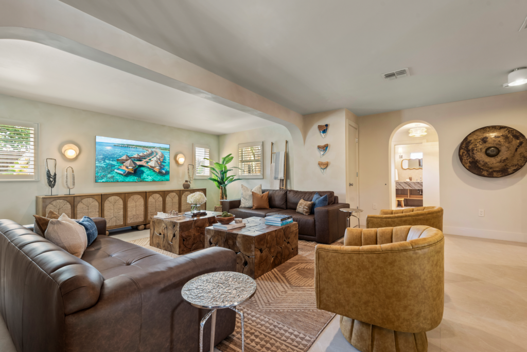 Bright open concept living room with leather sofas, wicker chairs, and coastal decor.